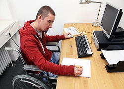 fotografía en la que se a una persona en silla de ruedas trabajando en un despacho, delante de un ordenador